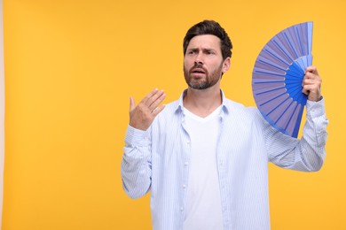 Photo of Unhappy man with hand fan suffering from heat on orange background. Space for text
