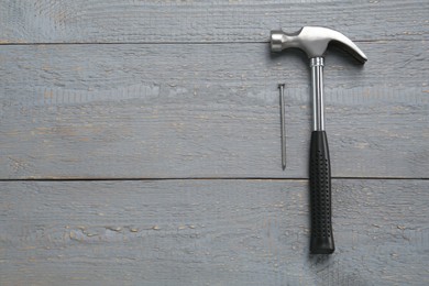 Photo of Hammer and metal nail on grey wooden table, flat lay. Space for text