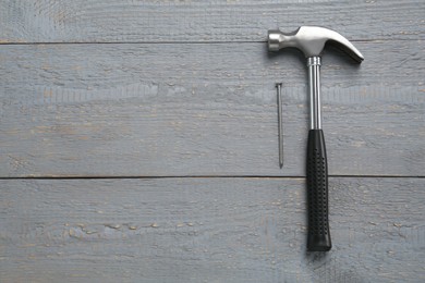 Hammer and metal nail on grey wooden table, flat lay. Space for text