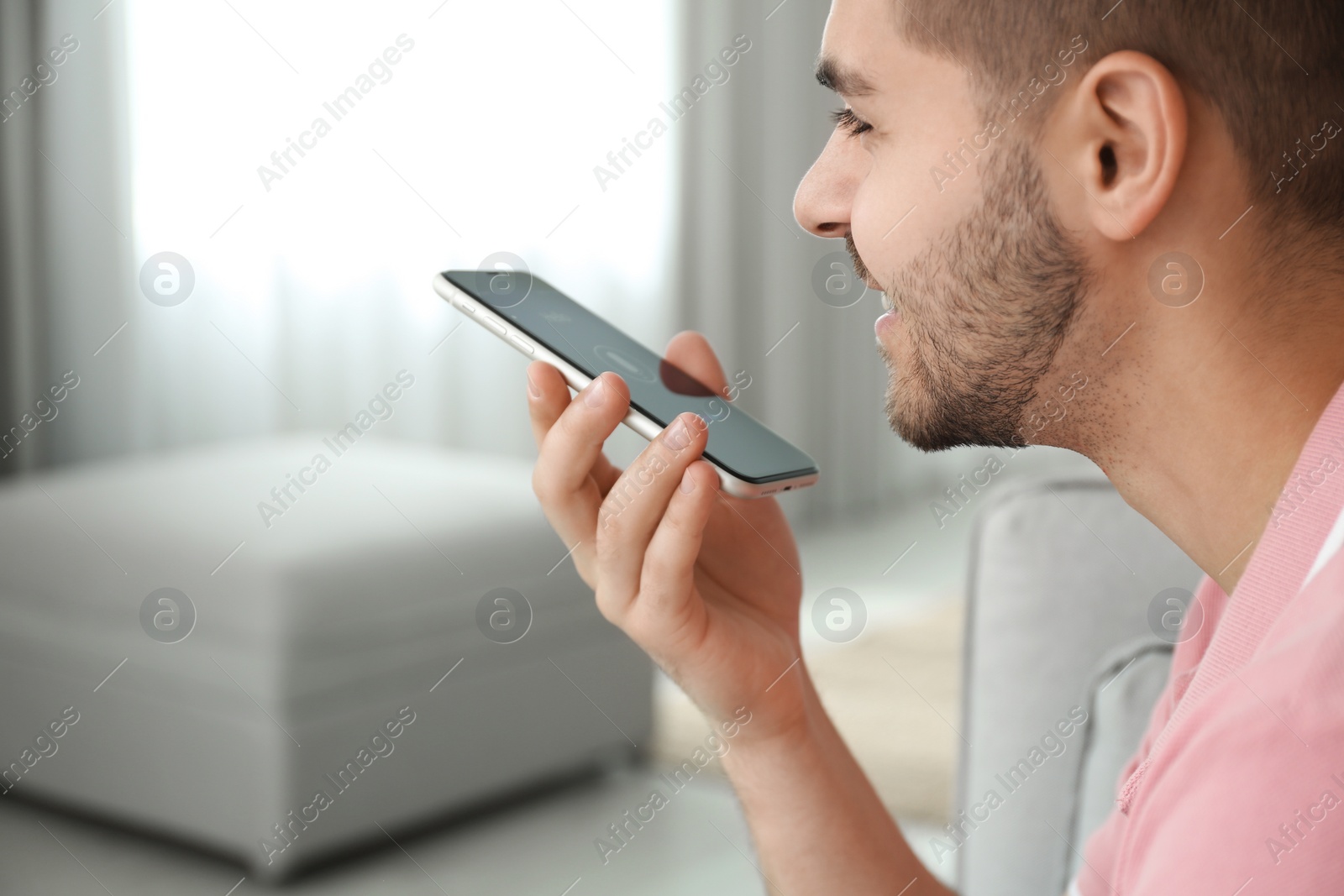 Photo of Young man using voice search on smartphone indoors