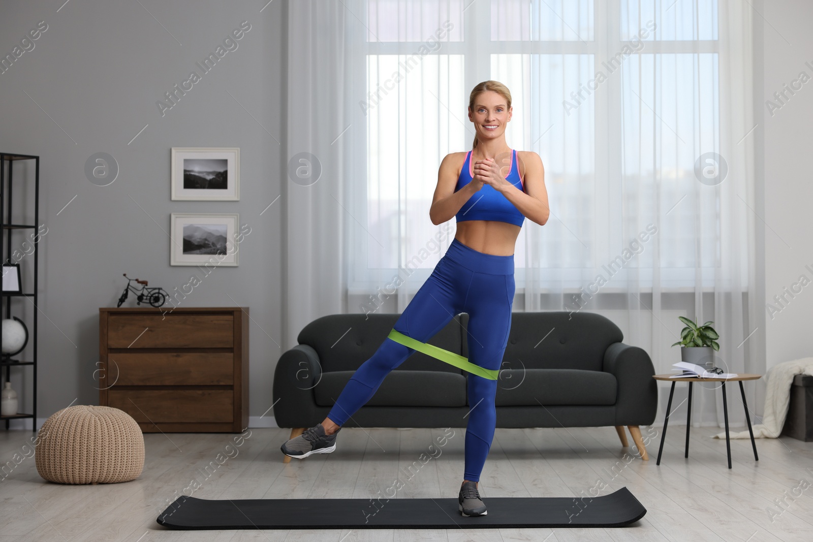 Photo of Athletic woman doing exercise with fitness elastic band on mat at home