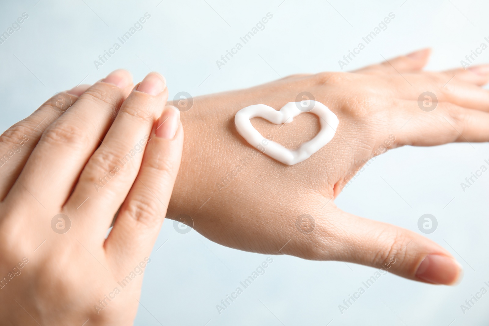 Photo of Woman applying hand cream on light background, closeup