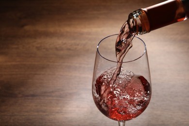 Pouring rose wine from bottle into glass on wooden table, closeup. Space for text