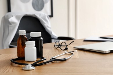 Photo of Bottles with medicaments, laptop and stethoscope on table indoors, space for text. Modern medical office interior