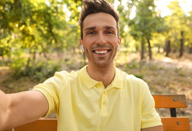 Young man with wireless earphones taking selfie in park