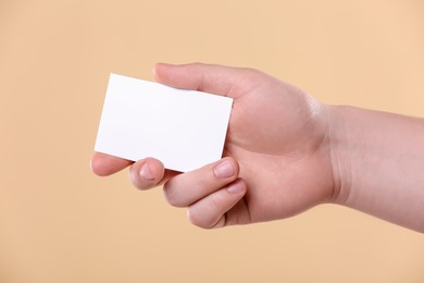 Man holding paper card on pale orange background, closeup. Mockup for design