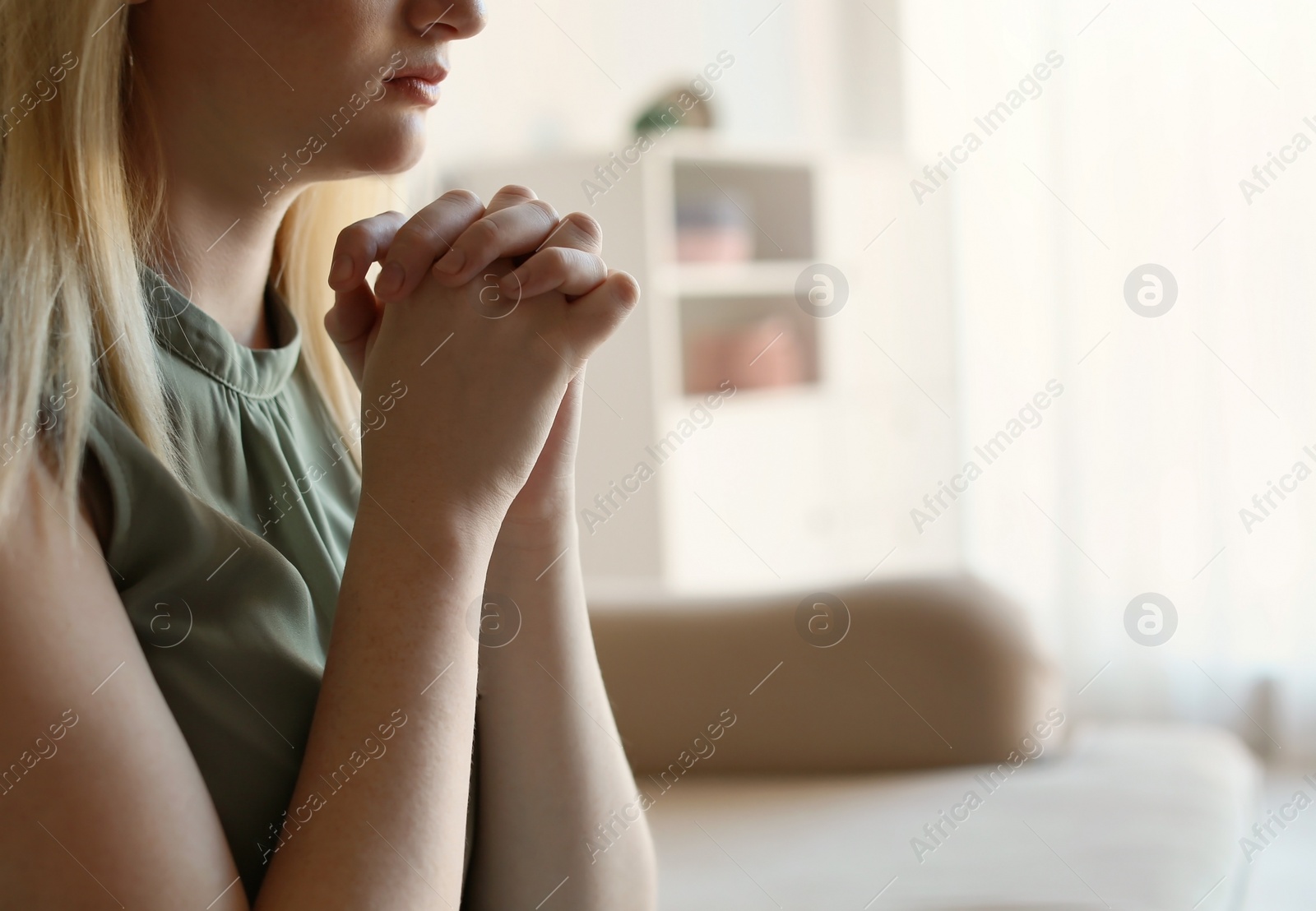 Photo of Religious young woman praying at home. Space for text