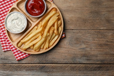 Photo of Delicious fresh french fries and different sauces on wooden table, top view. Space for text
