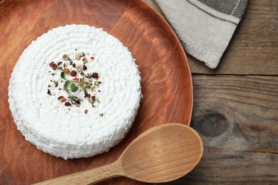 Photo of Wooden plate of fresh cottage cheese with spice and microgreens on table, top view