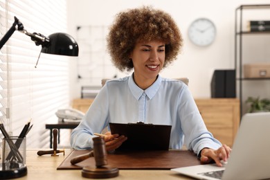 Photo of Notary with clipboard using laptop at workplace in office