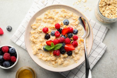 Photo of Bowl of oatmeal porridge served with berries on light grey table, flat lay