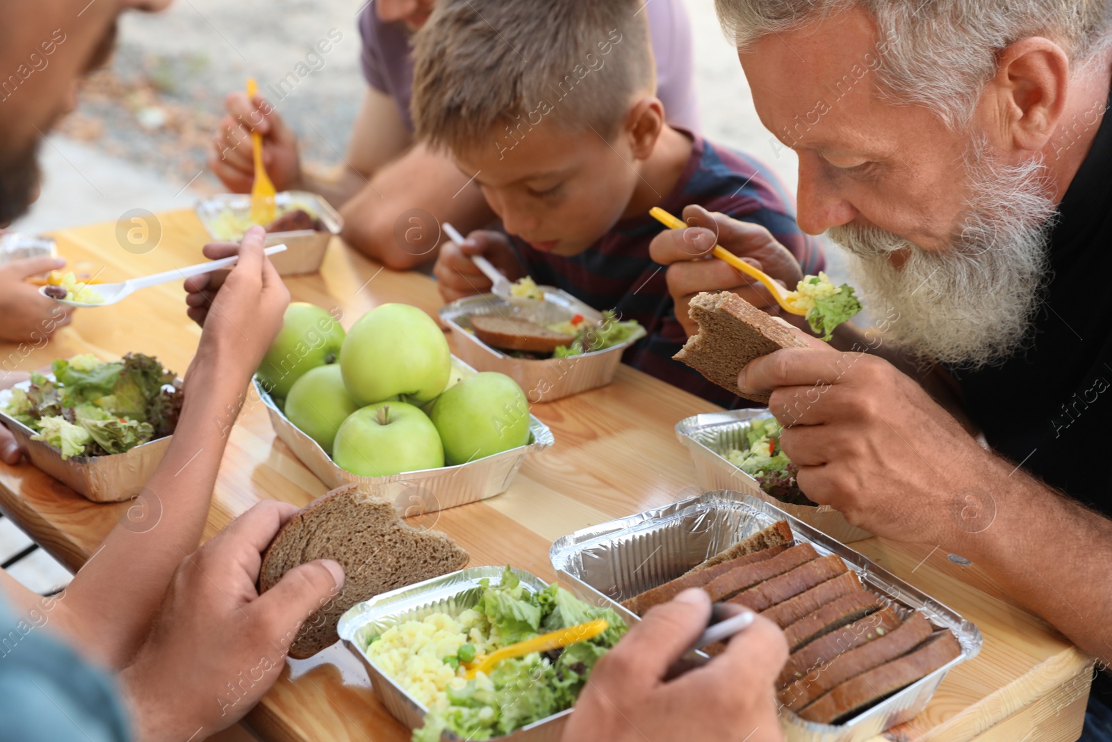 Photo of Poor people eating food at wooden table outdoors