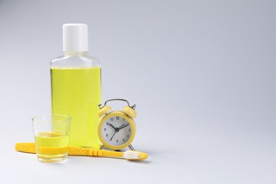 Photo of Fresh mouthwash in bottle, glass, toothbrush and alarm clock on grey background. Space for text