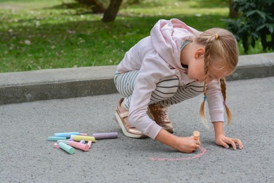 Little child drawing rainbow with chalk on asphalt