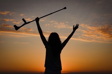 Photo of Woman holding elbow crutch outdoors at sunrise, back view. Healing miracle