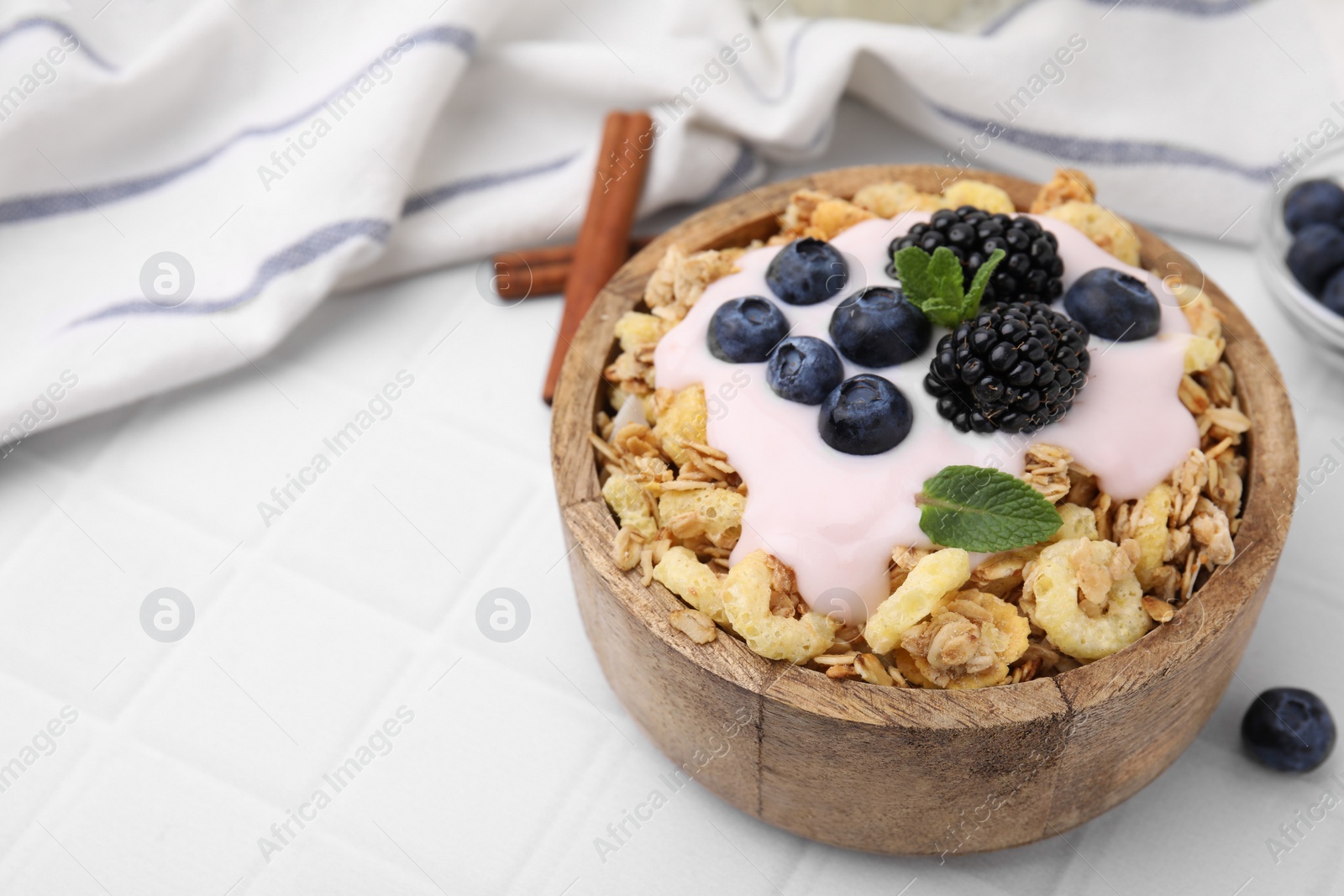 Photo of Tasty granola, yogurt and fresh berries in bowl on white tiled table, closeup with space for text. Healthy breakfast