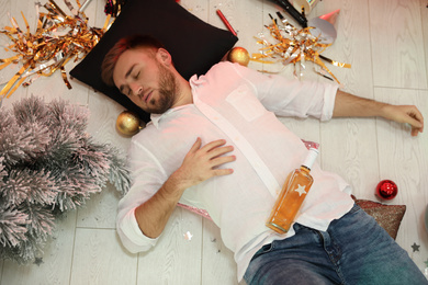 Photo of Drunk man sleeping on floor in messy room after New Year party, above view