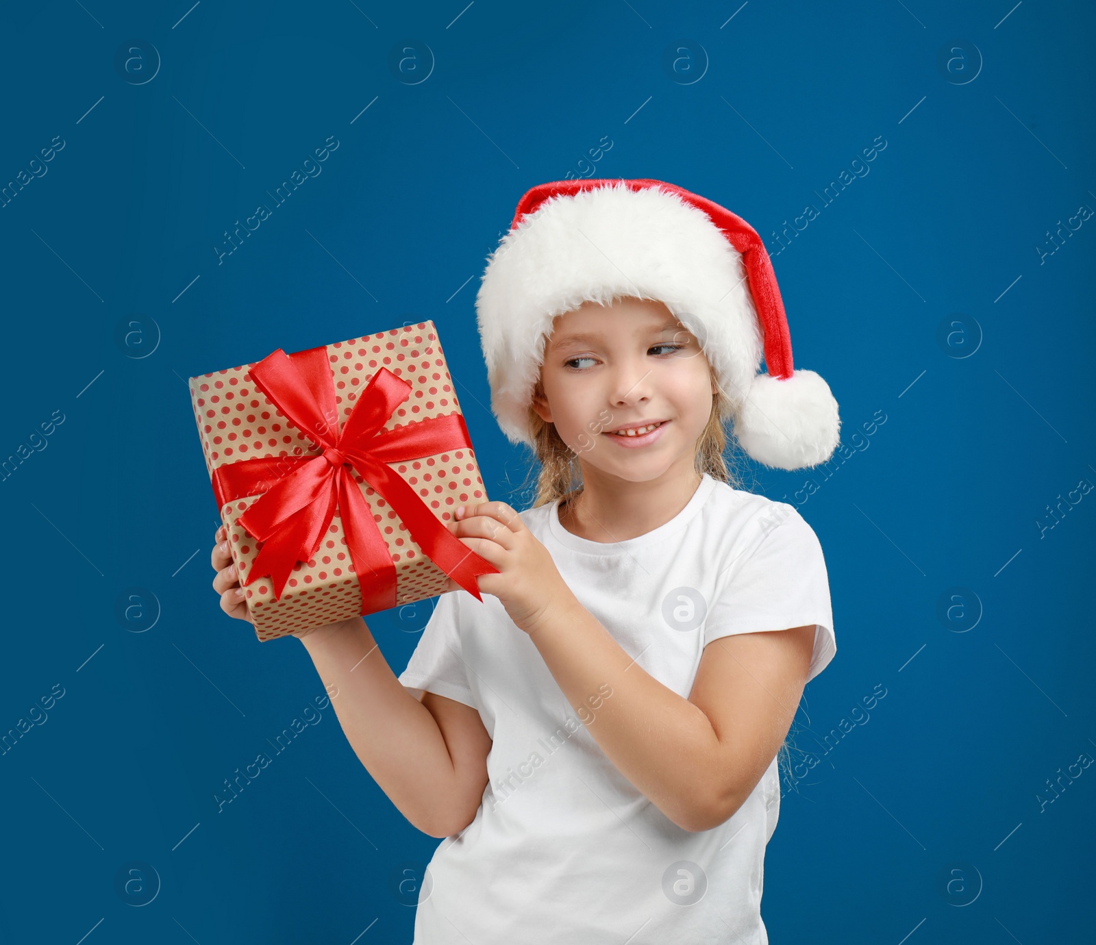 Photo of Cute little child wearing Santa hat with Christmas gift on blue background