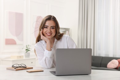 Photo of Happy woman with laptop at white table in room