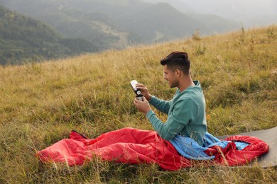 Photo of Man with thermos in sleeping bag on hill, space for text