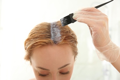 Photo of Young woman applying hair dye on roots against light background, closeup