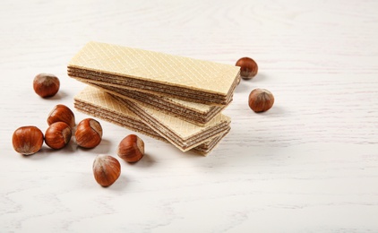 Photo of Delicious wafers with hazelnuts on white wooden background