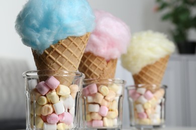 Sweet cotton candies in waffle cones and marshmallows on blurred background, closeup