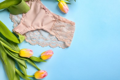 Photo of Elegant beige women's underwear and beautiful tulips on light blue background, flat lay. Space for text