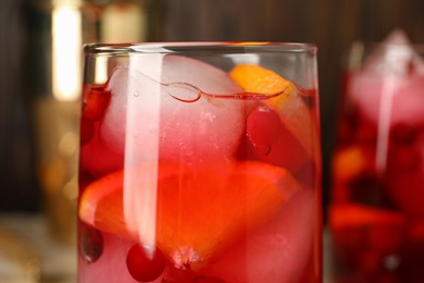 Photo of Tasty cranberry cocktail with ice cubes and orange in glass on table, closeup