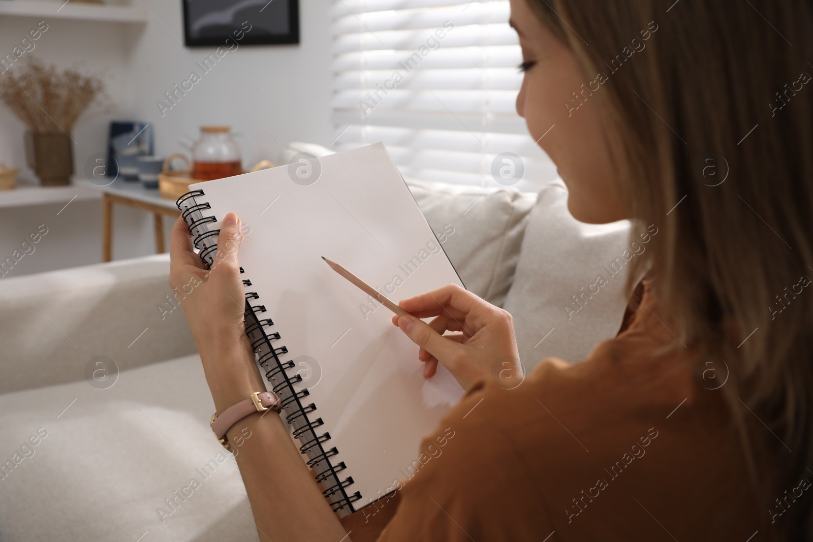 Photo of Young woman drawing in sketchbook with pencil at home