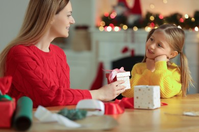 Photo of Christmas presents wrapping. Mother and her little daughter decorating gift boxes with ribbon at home