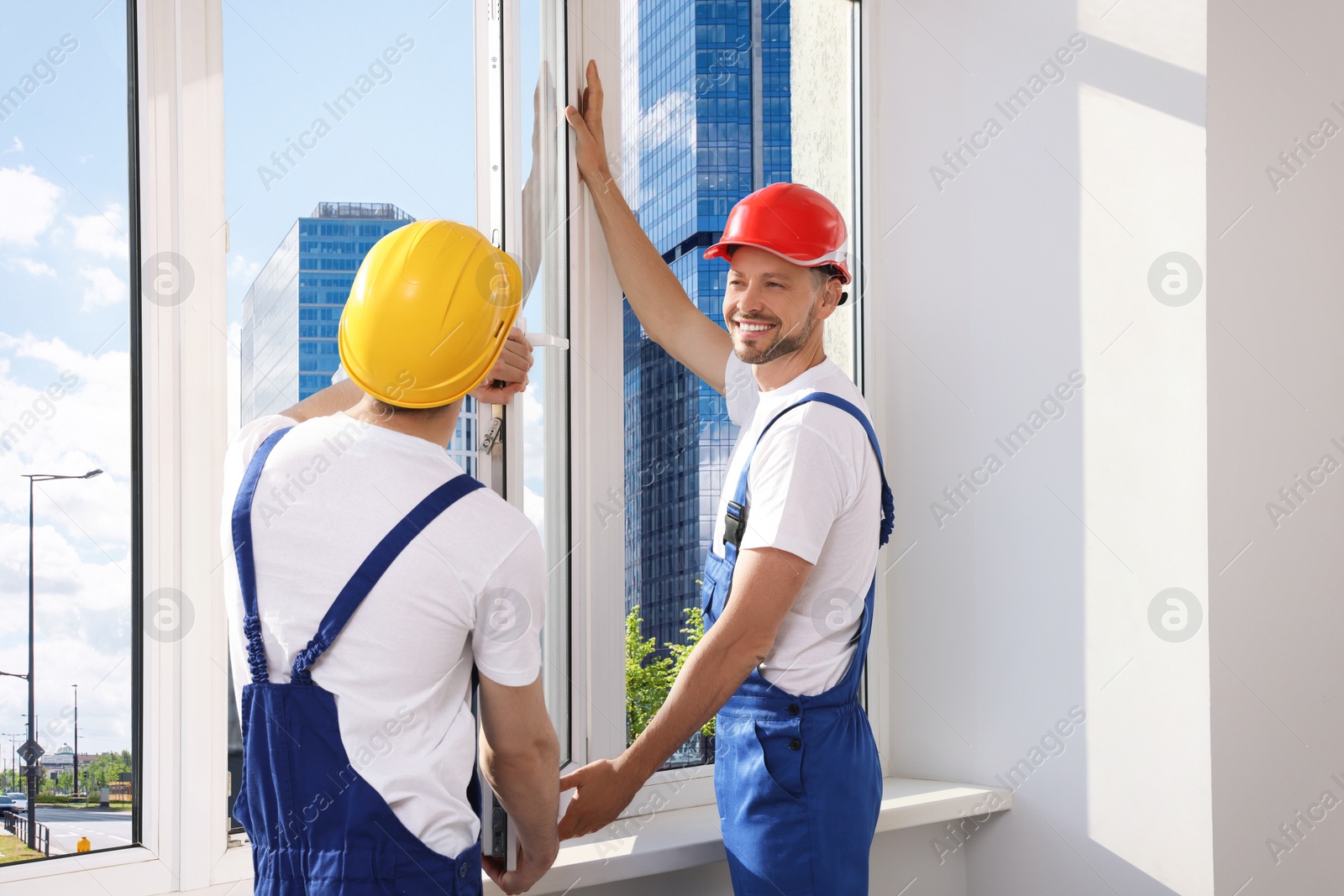 Photo of Workers in uniform installing plastic window indoors