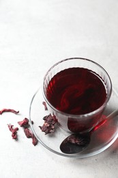 Photo of Aromatic hibiscus tea in glass, dried roselle calyces and spoon on light table, above view