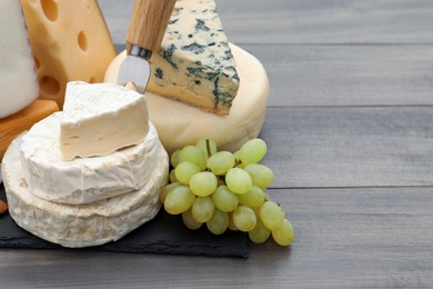 Photo of Different types of delicious cheeses and grapes on wooden table. Space for text