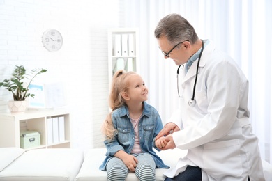 Doctor checking little girl's pulse with fingers in hospital. Space for text