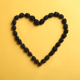Photo of Heart shaped frame made of fresh blackberries on yellow background, top view. Space for text