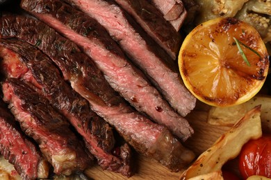 Photo of Delicious grilled beef with vegetables, lemon and spices on table, top view