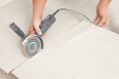 Worker cutting tiles with circular saw indoors, closeup