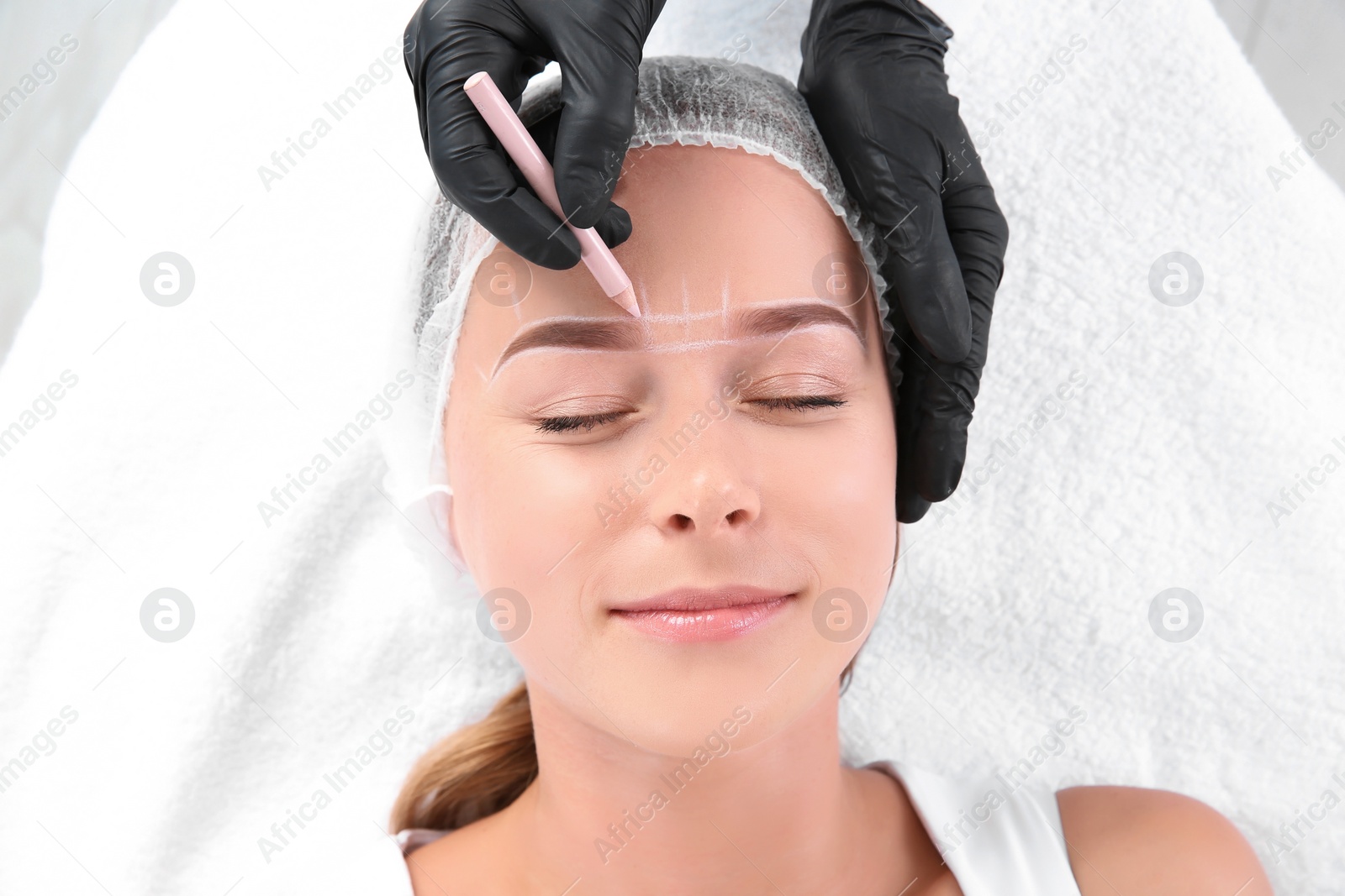 Photo of Young woman undergoing eyebrow correction procedure in salon, top view