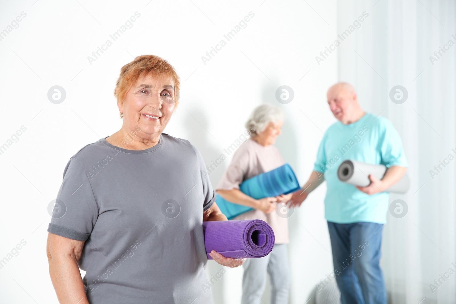Photo of Elderly woman with yoga mat indoors. Space for text