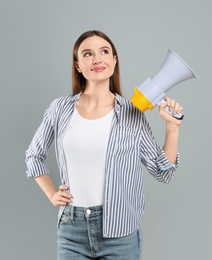 Young woman with megaphone on light grey background