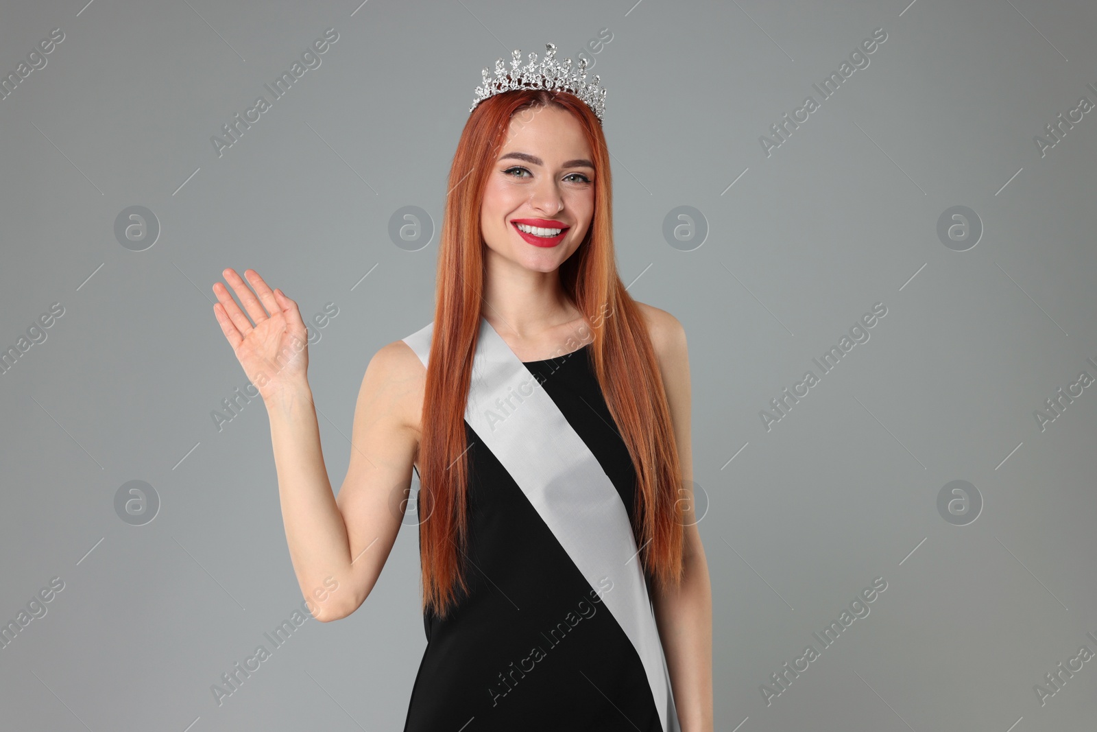 Photo of Beautiful young woman with tiara and ribbon in dress on light grey background. Beauty contest