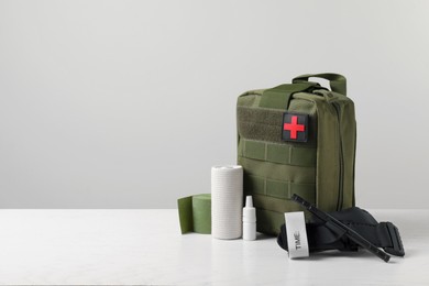 Photo of Military first aid kit, tourniquet, drops and elastic bandage on white table, space for text