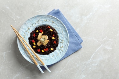 Photo of Plate with cooked brown rice and chopsticks on table, top view. Space for text