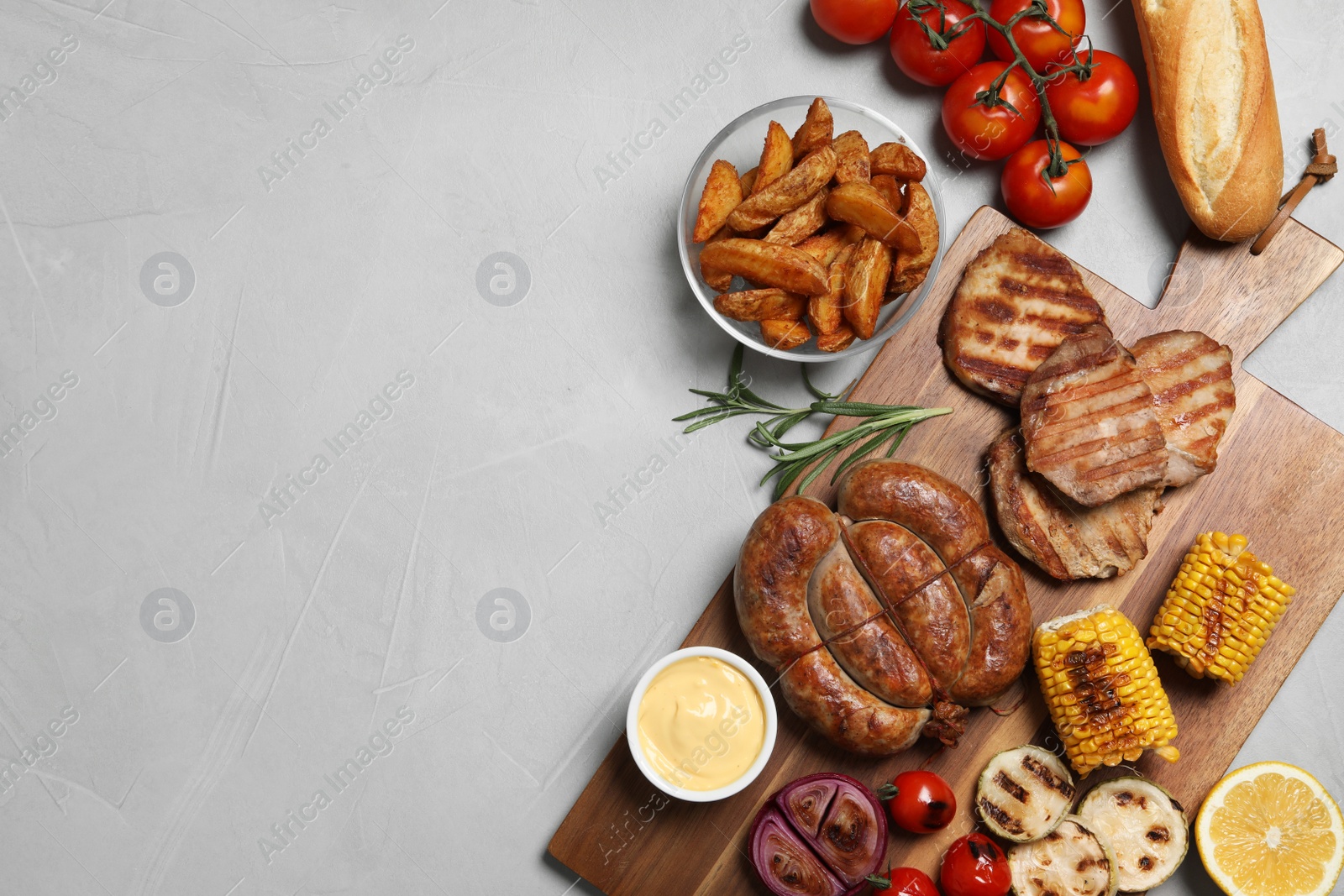 Photo of Flat lay composition with barbecued meat and vegetables on light table. Space for text