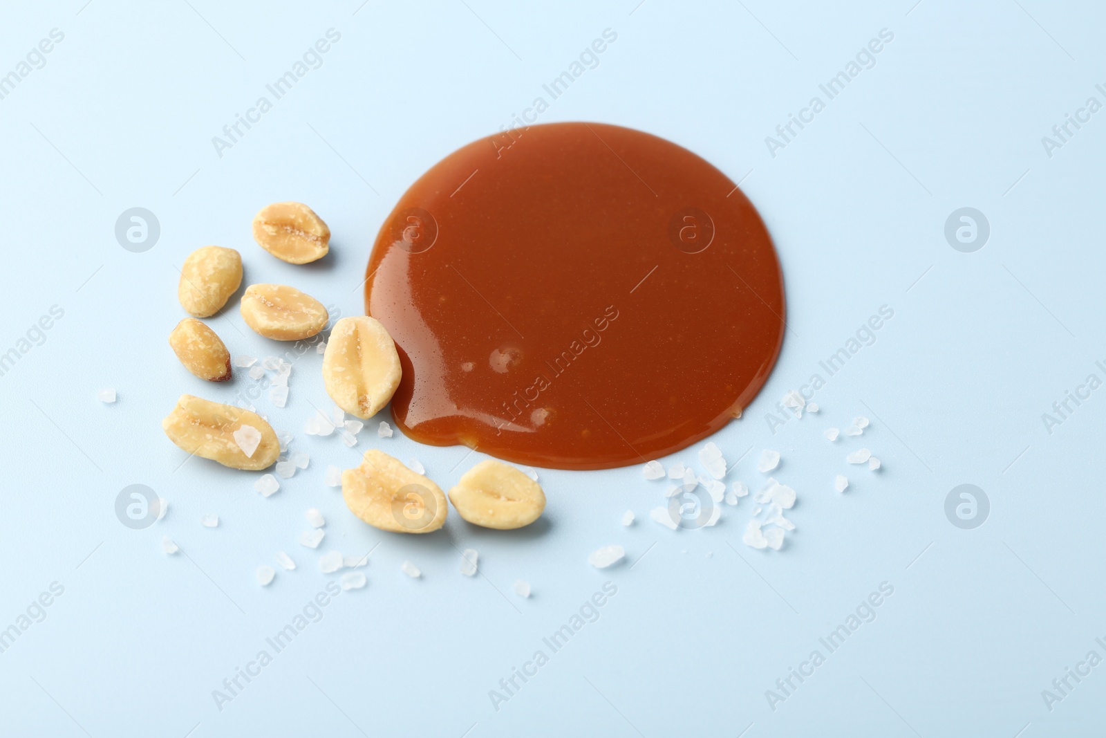 Photo of Smear of tasty salted caramel, peanuts and salt on light blue background, above view