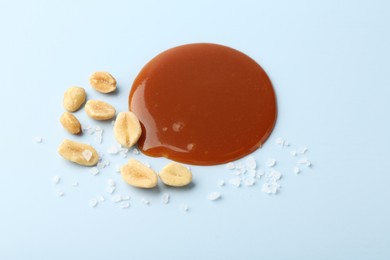 Photo of Smear of tasty salted caramel, peanuts and salt on light blue background, above view