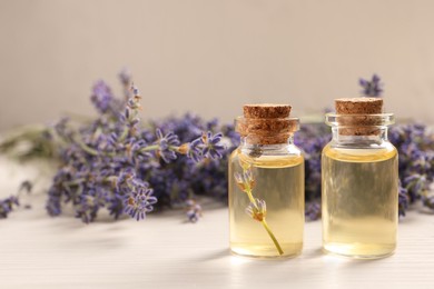 Photo of Essential oil and lavender flowers on white wooden table, closeup. Space for text