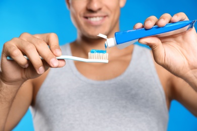 Photo of Man applying toothpaste on brush against blue background, closeup