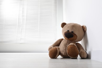 Photo of Cute lonely teddy bear on floor in empty room. Space for text